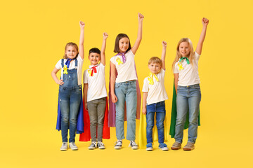 Fototapeta premium Little children dressed as superheroes with gold ribbons on color background. Childhood cancer awareness concept