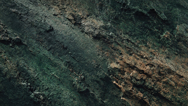 A rugged, dark green and earthy brown textured rock surface, showcasing natural striations, organic patterns, and weathered details.
