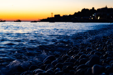 Pebble beach at beautiful sunset with waves and twilight sky, scenic coastal seascape for summer travel