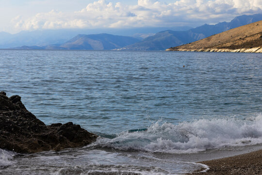 Scenic view near Himare on the Albanian Riviera, with waves, rocks, clouds, and distant mountains