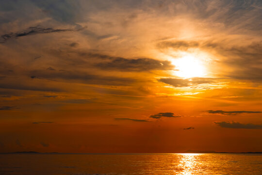Dramatic sunset over the sea with glowing sun descending into clouds above distant islands