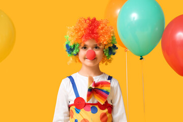 Funny little boy in clown costume with balloons on yellow background. April Fools Day celebration