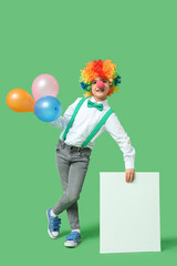 Funny little boy in clown wig with nose holding balloons and blank poster on green background. April Fools Day celebration