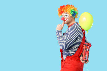 Young man as crazy clown with dynamite and balloon showing silence gesture on blue background