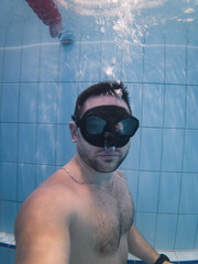 Underwater portrait of a male freediver wearing a black mask during a breath-holding and static apnea training session.