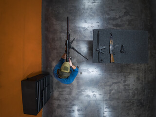 Top-down view of a rifleman wearing protective gear and a helmet, aiming a precision rifle from a bipod during a tactical shooting session.