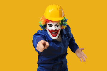 Screaming young man as clown in coverall and helmet pointing at someone on yellow background