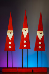 Winter Christmas decorative ornaments: three whimsical gnomes as a symbol of good luck in the new year. Handmade wooden gnomes with red hats on a wooden table, closeup