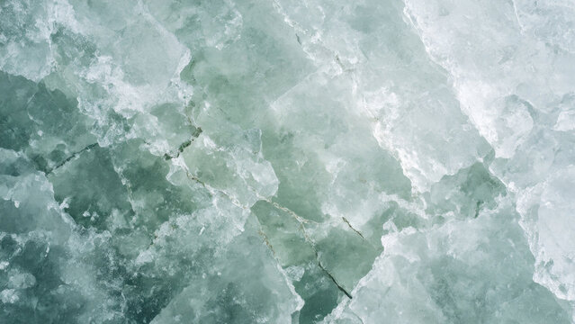 An abstract close-up of fractured ice, showcasing varying translucent textures, cracks, and beautiful shades of teal, green, and white.