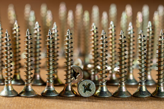 Many golden metal self tapping screws for construction work, closeup. New metal fasteners self tapping screws for connecting wooden elements. Row of screws on a wooden table