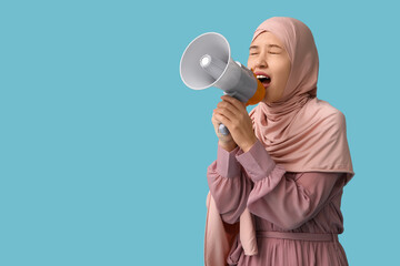 Young Asian Muslim woman shouting into megaphone on blue background. National Be Heard Day