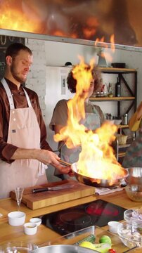 Vertical low angle shot of profesional chef showing his students how to flambe dish during master class