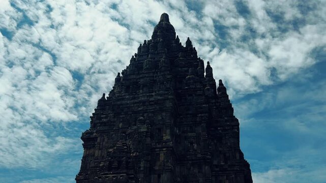 View of the ancient Prambanan Temple, a Hindu temple complex in Yogyakarta, Indonesia. The temple rises above the green foliage under a blue sky. The towers cast shadows on a sunny day. 4К
