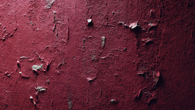 A textured close-up of a dark red wall with extensive peeling paint, revealing a lighter underlayer, showcasing age and decay.