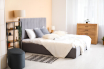 Blurred view of bedroom with big bed, shelf unit and lamps