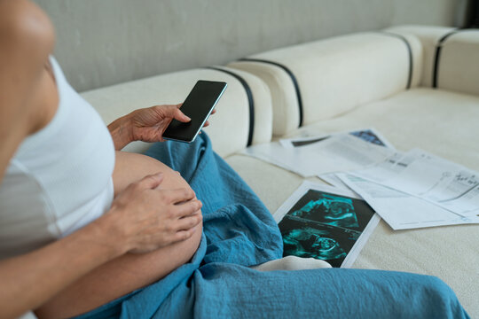 Expectant pregnant woman checks medical test results and ultrasound through a phone app in a calm home setting, telemedicine and assistance with remote medical consultation