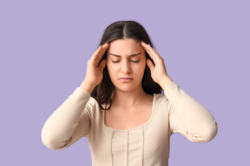 Young woman suffering from headache on lilac background