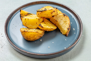Roasted potato wedges with golden crust and coarse salt, presented on a minimalist blue plate. Clean, simple food styling and natural light.
