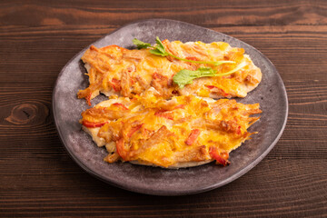 baked chicken meat with cheese and tomatoes on brown wooden. side view, close up