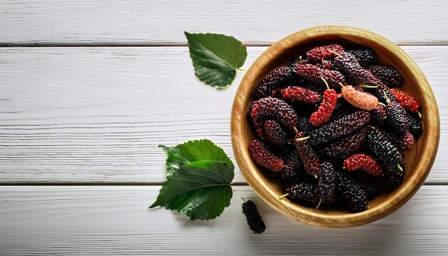 fresh and ripe mulberries in a wooden bowl on a white wooden table