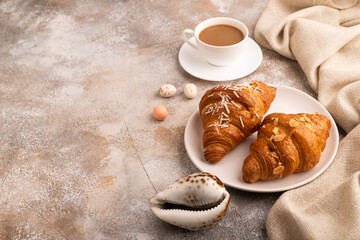 Croissant on white plate on brown concrete background, cup of coffee, side view, copy space
