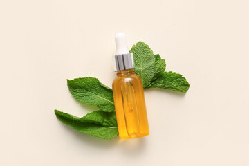 Bottle of essential mint oil and green leaves on beige background