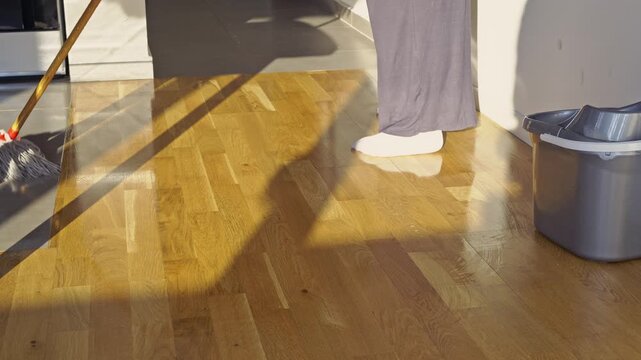 A person meticulously mops a beautiful wooden floor, creating a sparkling clean surface.