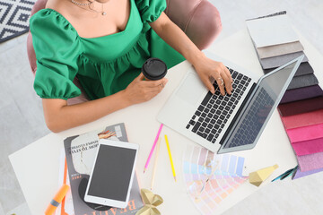 Young graphic designer with laptop and coffee working at table in office, top view