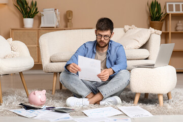 Fototapeta premium Young man in debt with paper sitting on floor at home