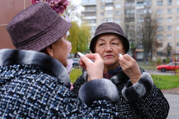 adult elderly woman on the street in a hat and coat in front of a mirror. High quality photo