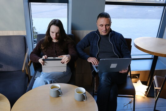 Businesspeople having a conversation at a table outside a cafe, discussing work and using a tablet. father and daughter working on laptops in a cafe