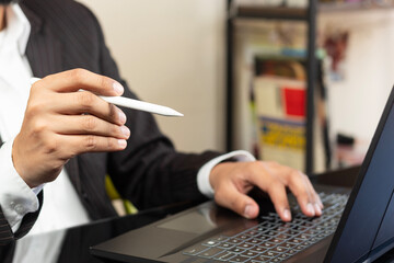 a right hand of a business man on suit pointing to the screen of a laptop