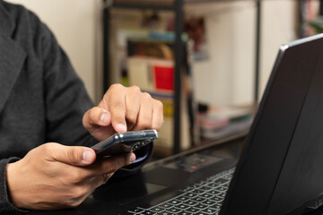 Close up to a modern business man pointing with his left index finger to a smartphone display over a laptop at the left side of the screen