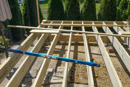 A long carpenter's level on the wooden frame of a backyard deck that is being built