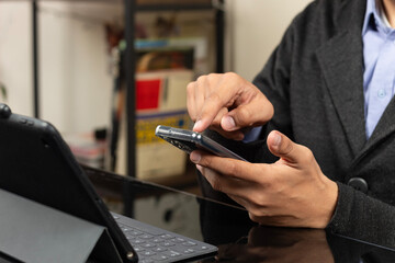 a modern CEO pointing with his index finger to the display of a smartphone in front of a tablet with keyboard
