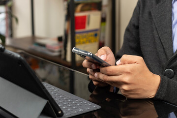 a modern CEO typing with both thumbs on a smartphone in front of a tablet with keyboard