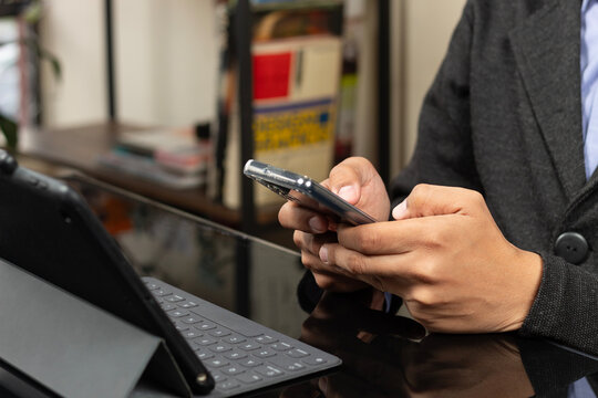 a modern CEO typing with both thumbs on a smartphone in front of a tablet with keyboard