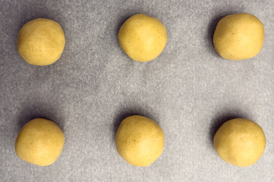 Six round dough balls arranged on parchment paper, ready for baking, showcasing the preparation process for delicious homemade cookies in a kitchen setting - Powered by Adobe