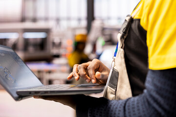 Industrial automation expert ensures efficiency in smart manufacturing plant, using industry 4.0 software on laptop. African american engineer evaluates robotic arms and systems in automated factory.