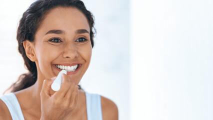 A woman with dark hair smiles as she applies lip balm in front of a mirror. The bright room reflects a clean and fresh atmosphere, creating a joyful moment of self-care and beauty.