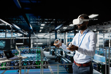 Server hub male programmer using virtual reality technology to simulate AI neural network systems. Young man in data center using VR goggles tools to oversee futuristic AI visualization.