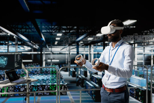 Server hub male programmer using virtual reality technology to simulate AI neural network systems. Young man in data center using VR goggles tools to oversee futuristic AI visualization.