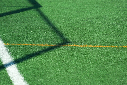 Green synthetic grass, artificial turf sports field with yellow and white lines and soccer goal shadow