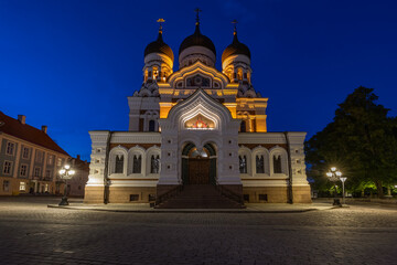 The brilliantly illuminated Alexander Nevsky Cathedral stands grandly against a deep blue evening sky in Tallinn, its ornate Russian Revival architecture dominating the square.