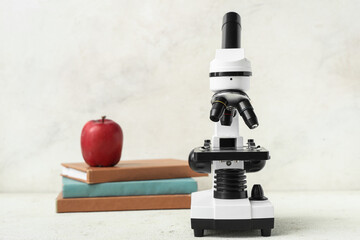 Microscope, school books and apple on light background