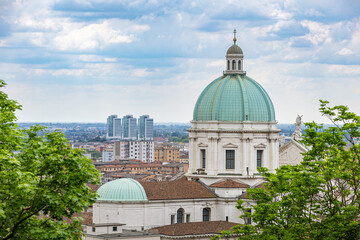 Fototapeta premium View of the green dome of the Sanctuary of Santa Maria delle Grazie (or a similar church) overlooking the cityscape of Brescia, with modern high-rise buildings visible in the distance