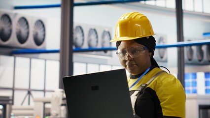 Woman conducts routine inspections in industry 4.0 solar panels plant using laptop. Engineer in photovoltaics smart factory testing equipment and reviewing system metrics using notebook