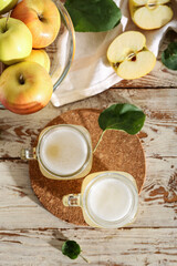 Mason jars of fresh apple kvass and glass bowl with fruits on white wooden background