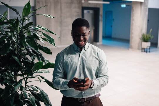 Black man smiling checking smartphone in modern office - Powered by Adobe