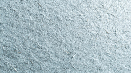 Fototapeta premium A close-up texture of light blue fibrous paper, exhibiting a rough, organic surface with visible plant fragments.